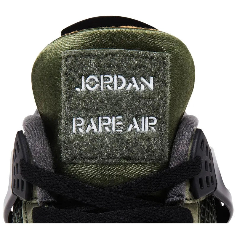 Undefeated x Air Jordan 4 (2025 reissue) in olive nubuck with black wings/eyelets, Nike Air heel tab, orange lining, Velcro tongue patches, off-white midsole, visible heel Air unit.